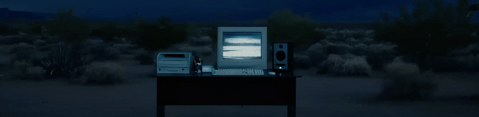 A computer monitor placed on a desk in a vast desert landscape under a clear blue sky.